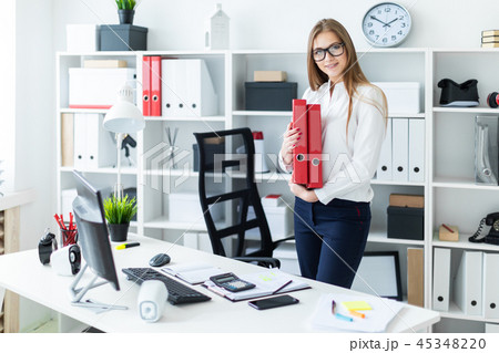 A young girl stands near a computer Desk and holds a folder with documents A young girl stands near a computer Desk and holds a folder with documents 45348220