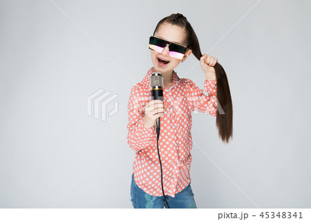 Girl on a gray background singing into the microphone. Girl on a gray background singing into the microphone. 45348341