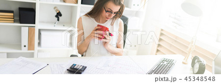 A young girl in the office holds a pink marker, a red mug and works with documents. 45348548