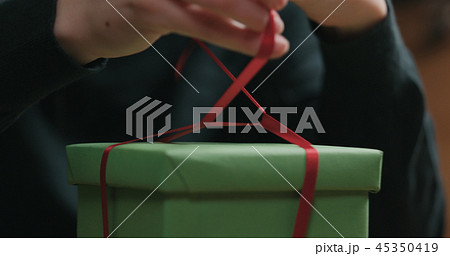 Closeup shot of female hands tying red ribbon bow on green paper gift box 45350419