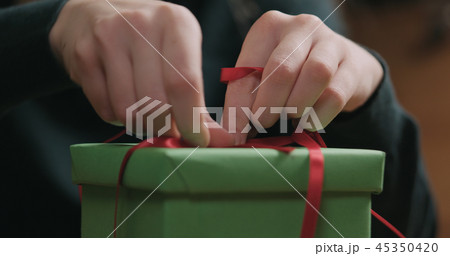 Closeup shot of female hands tying red ribbon bow on green paper gift box 45350420