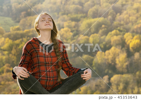 Pregnant woman sits on a hill with her eyes closed 45353643