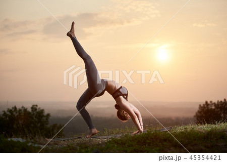 Attractive slim young woman doing yoga exercises outdoors on copy space background of beautiful sky. 45354421