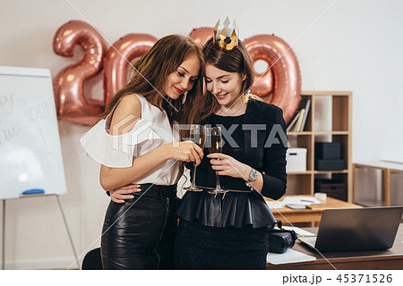 Two girls with glasses of champagne hugging and celebrating Christmas in the office Two girls with glasses of champagne hugging and celebrating Christmas in the office 45371526