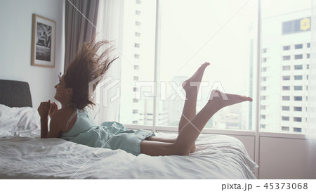 Happy woman jumping on bed at home and relaxing by the panoramic window with amazing city view Happy woman jumping on bed at home and relaxing by the panoramic window with amazing city view 45373068