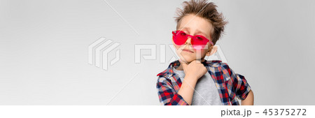 A handsome boy in a plaid shirt, gray shirt and jeans stands on a gray background. A boy in red 45375272