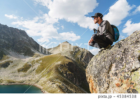 A bearded hipster tourist in sunglasses with a backpack sits on the edge of a cliff high in the 45384538