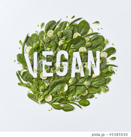 Round composition of different green vegetables with vegan paper lettering on a gray background with 45385030