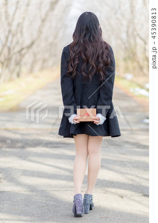 後ろ手にプレゼントボックスを持つ若い女性 45390813