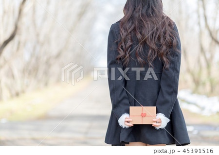 後ろ手にプレゼントボックスを持つ若い女性 45391516
