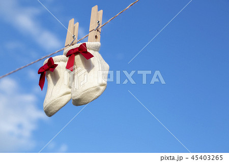 青空に木製洗濯挟みで吊るされた赤いリボンの新生児用靴下。赤ちゃん、育児、出産、幸せ、愛イメージ 45403265
