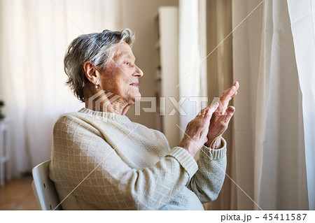 A portrait of a senior woman sitting at home, looking out of a window. 45411587