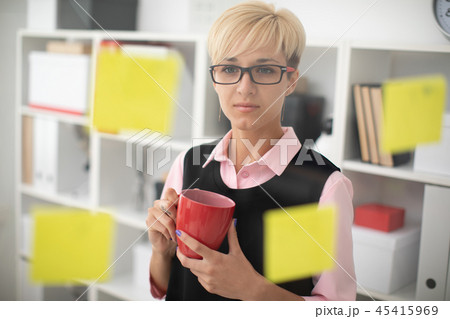 A young girl stands in the office near a transparent Board with stickers and holds a red Cup in her A young girl stands in the office near a transparent Board with stickers and holds a red Cup in her 45415969