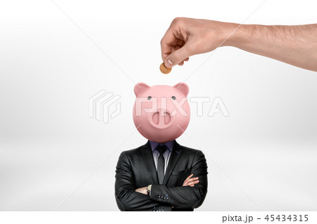Hand inserting coin into piggy bank head of a businessman on white background Hand inserting coin into piggy bank head of a businessman on white background 45434315