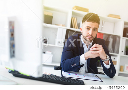 A young man sitting in the office at a computer Desk and working with documents. A young man sitting in the office at a computer Desk and working with documents. 45435200