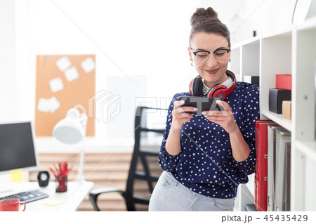 A young girl in glasses stands in the office on the floor of the rack and holds a phone in her hand 45435429