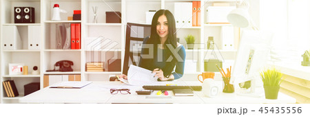 A young girl sits in the office at the table, holds a pen in her hand and fills out the documents. 45435556