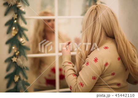 A pretty pregnant blonde hair woman in a Christmas sweater stands near the mirror. Winter spirit A pretty pregnant blonde hair woman in a Christmas sweater stands near the mirror. Winter spirit 45442110