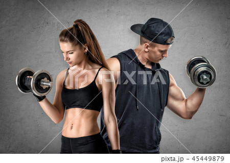 A young muscular woman and a fit man stand on a concrete background. 45449879