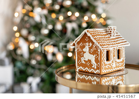 Gingerbread house on table. Defocused lights of Christmas tree. Morning in the bright living room 45451567