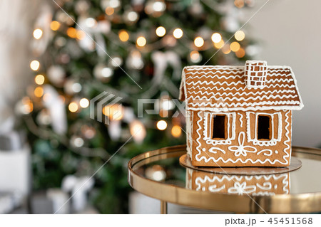 Gingerbread house on table. Defocused lights of Christmas tree. Morning in the bright living room Gingerbread house on table. Defocused lights of Christmas tree. Morning in the bright living room 45451568