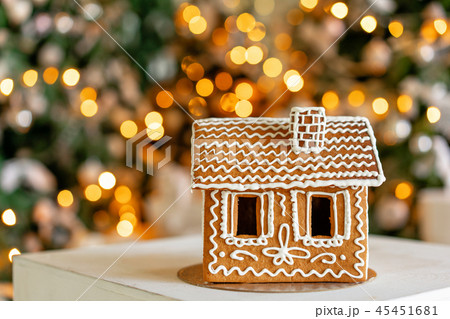 Gingerbread house on table. Defocused lights of Christmas tree. Morning in the bright living room Gingerbread house on table. Defocused lights of Christmas tree. Morning in the bright living room 45451681