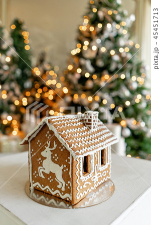 Gingerbread house on table. Defocused lights of Christmas tree. Morning in the bright living room Gingerbread house on table. Defocused lights of Christmas tree. Morning in the bright living room 45451713