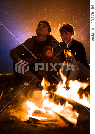 man plays guitar and woman about the fire 45476364