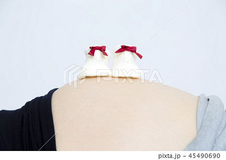 妊娠した大きなお腹の上に置かれた新生児用の靴下。妊娠,妊婦,臨月,期待,愛,幸福イメージ 45490690