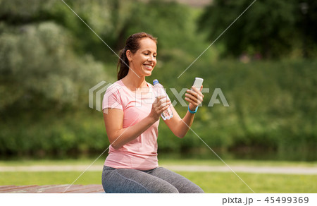 woman with smartphone drinking water in park 45499369