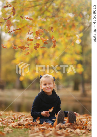 Beautiful young girl sist in leaves and throws them up. Colorful background. Happy little girl smile Beautiful young girl sist in leaves and throws them up. Colorful background. Happy little girl smile 45509015