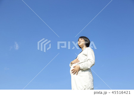 青空を背景に大きなお腹に希望を持って手を当てている臨月の妊婦の様子。妊娠、臨月、愛、楽しみ、幸せイメ 45516421