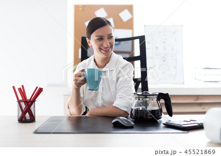 A young girl sitting at a table in the office and holding a Cup. 45521869