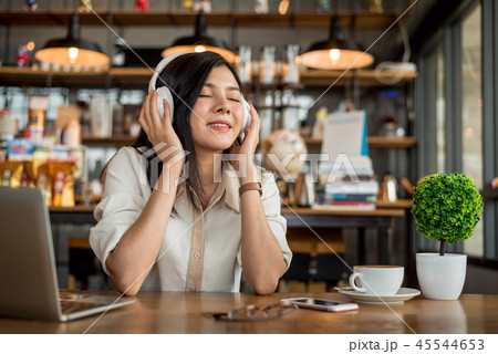 Happy Asian woman relaxing and listening music in coffee shop wi 45544653