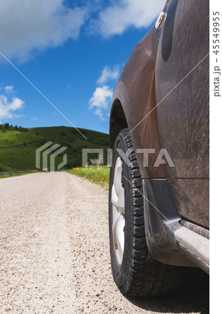 Close-up of a SUV wheel on an asphalt road outside the city against the green hills of blue sky and 45549955