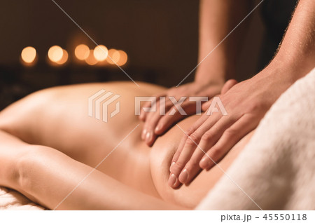 Close-up male hands doing healing massage with oil to a young girl in a dark cosmetology office 45550118