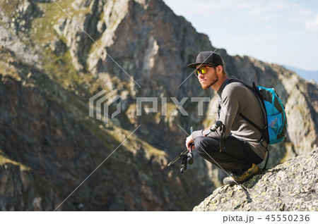 A bearded hipster tourist in sunglasses with a backpack sits on the edge of a cliff high in the A bearded hipster tourist in sunglasses with a backpack sits on the edge of a cliff high in the 45550236