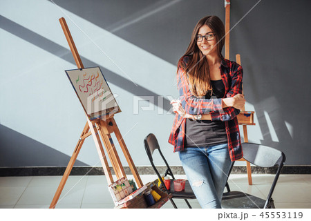 Pretty Pretty Girl artist paints on canvas painting on the easel. Studio black background. Long hair 45553119