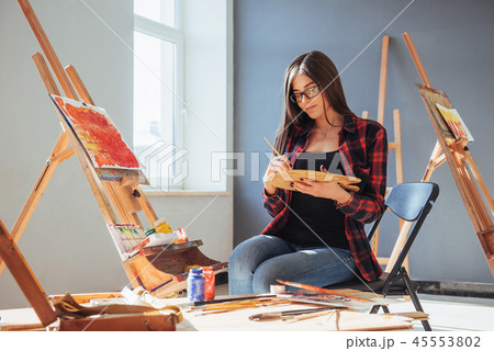 Dark-haired artist holding a brush in his hand and draws a picture on canvas. Thinks that draw on 45553802