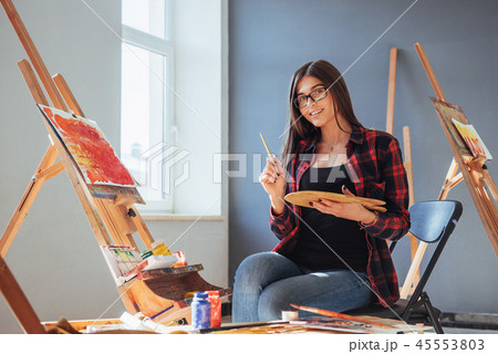 Dark-haired artist holding a brush in his hand and draws a picture on canvas. Thinks that draw on 45553803