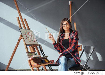 Dark-haired artist holding a brush in his hand and draws a picture on canvas. Thinks that draw on 45553836