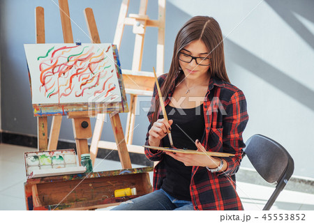 Creative pensive painter girl paints a colorful picture on canvas with oil colors in workshop 45553852