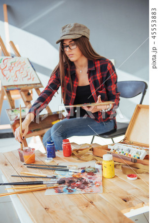Creative pensive painter girl paints a colorful picture on canvas with oil colors in workshop 45553883