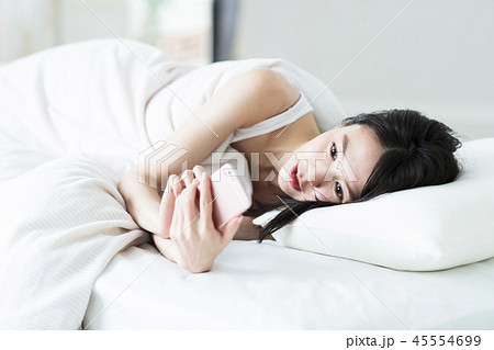 女性 寝起き スマホ 朝 起床 若い女性 かわいい ライフスタイルの写真素材