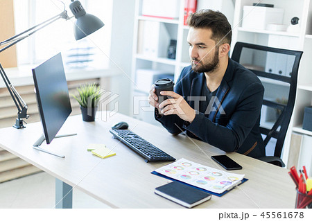 A young man working in the office at the computer and holding a glass of coffee. 45561678