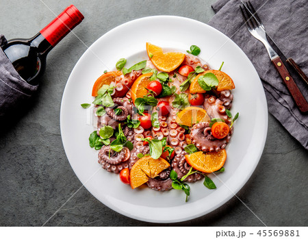 Whole octopus salad with orange, tomatoes and cress salad on white plate. Top view 45569881