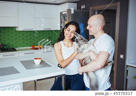 Happy young beautiful couple sitting at kitchen cat smiling. 45570317