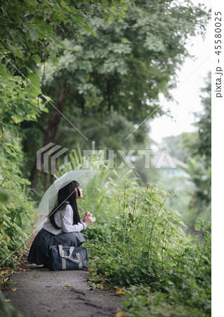 Portrait of Asian school girl walking with umbrella at nature walkway on raining 45580025