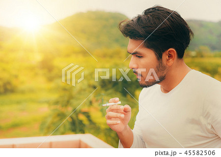 Young man smoking cigarette in the outdoors. 45582506