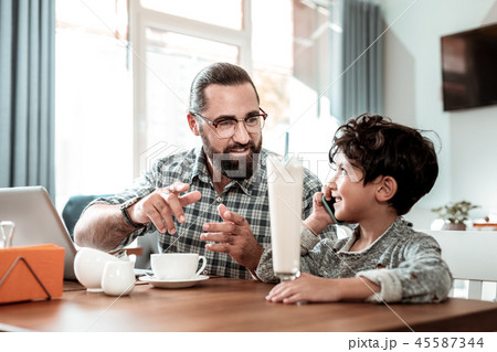 Bearded dark-haired father wearing glasses talking to his cute little son Bearded dark-haired father wearing glasses talking to his cute little son 45587344